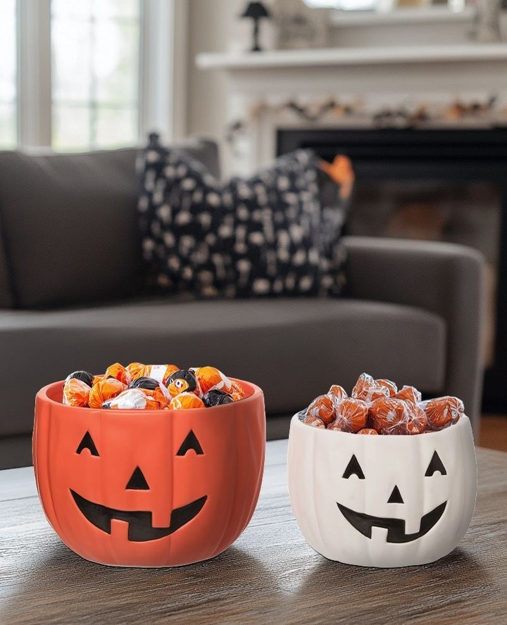 Orange and white pumpkin bowls filled with Halloween candy on coffee table.