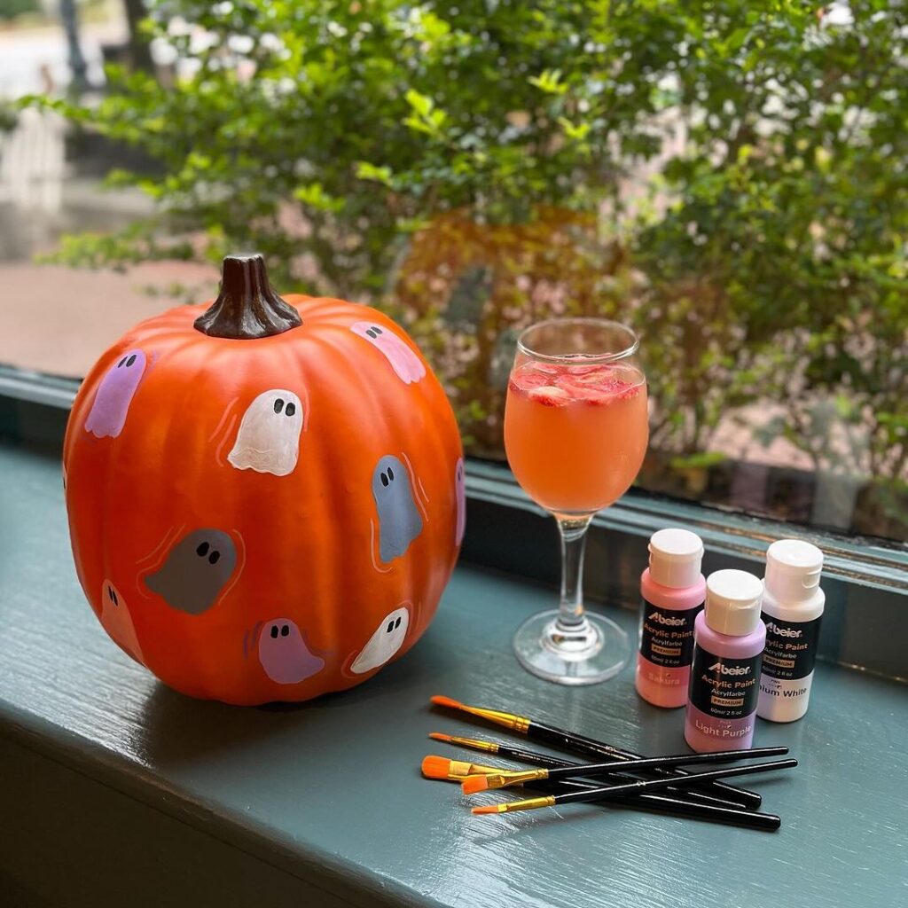 Painted pumpkin with ghosts beside cocktail and art supplies
