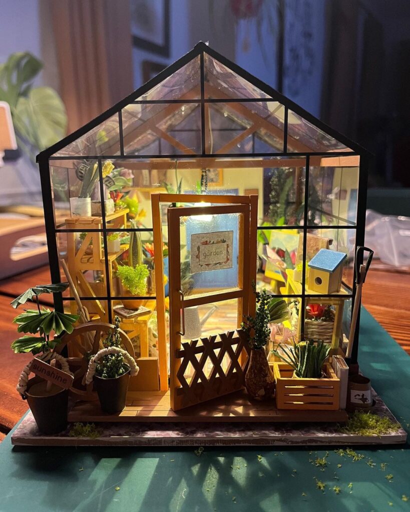 Illuminated miniature greenhouse dollhouse with tiny garden items.