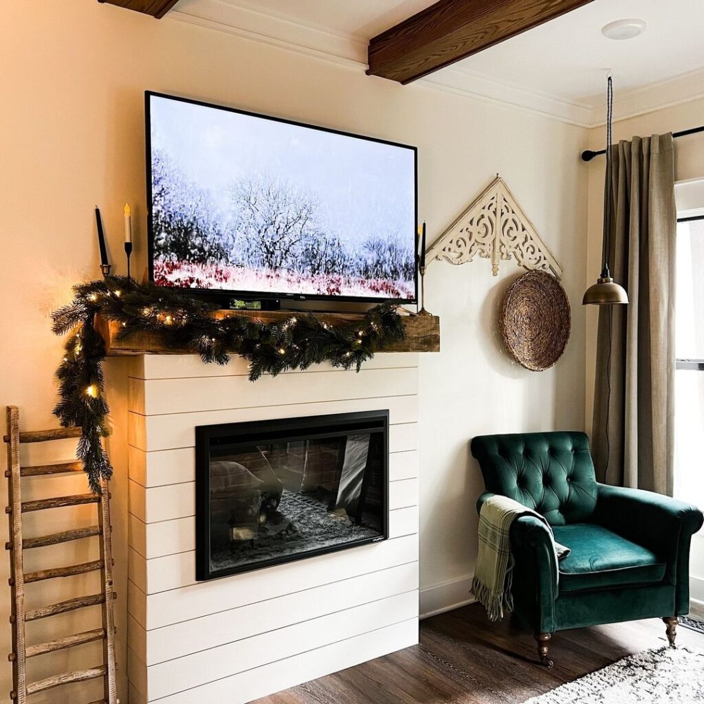 Cozy fireplace corner with green velvet chair and lit holiday garland