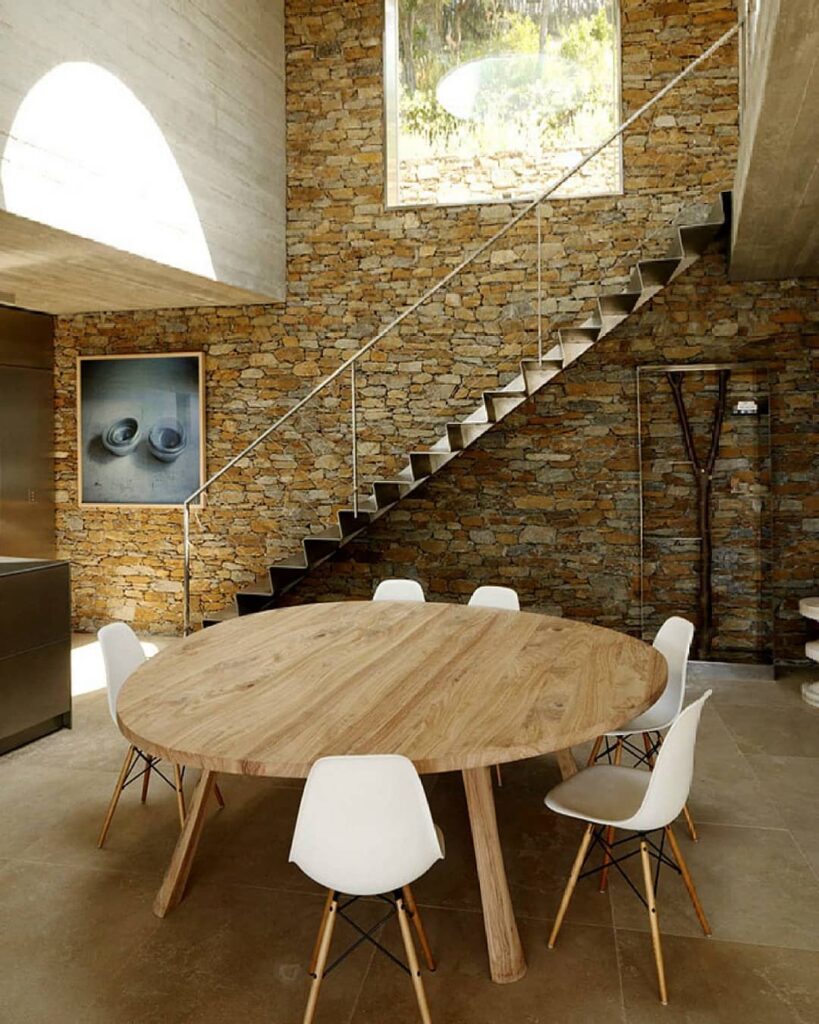 Round wooden table with white modern chairs against stone wall