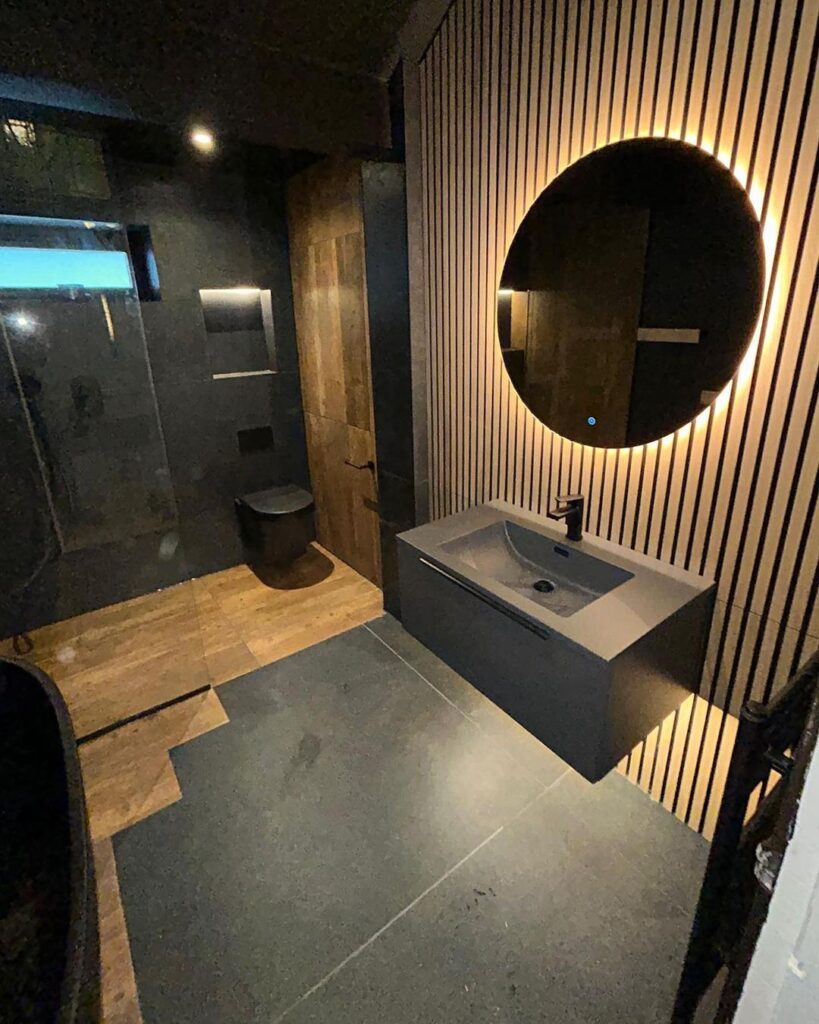 Modern dark bathroom with backlit mirror and floating sink. 