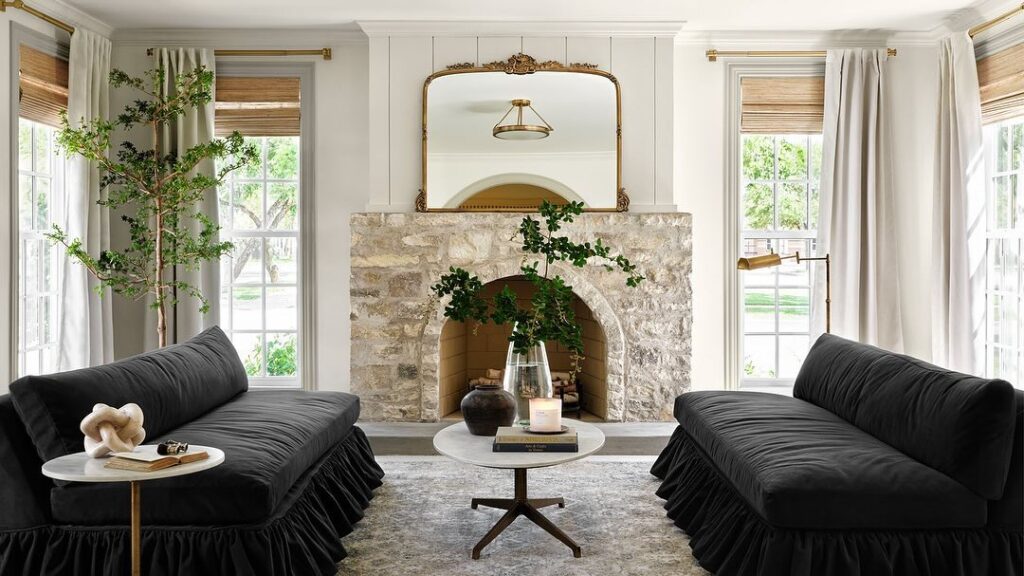 Living room with black sofas stone fireplace and large windows.