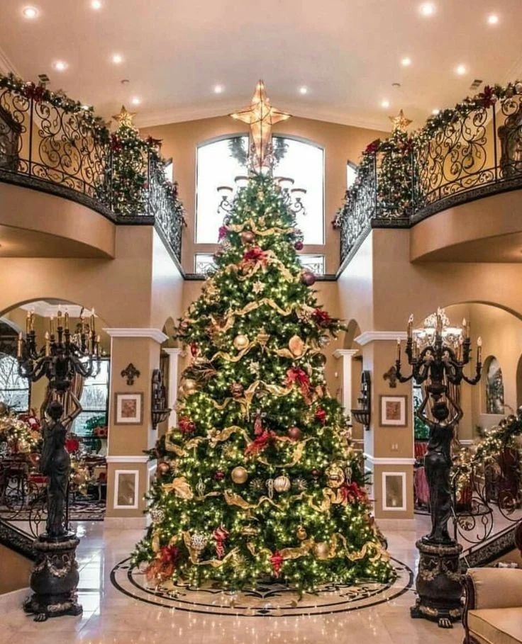 Towering Christmas tree between dual staircases with bronze statues and iron railings