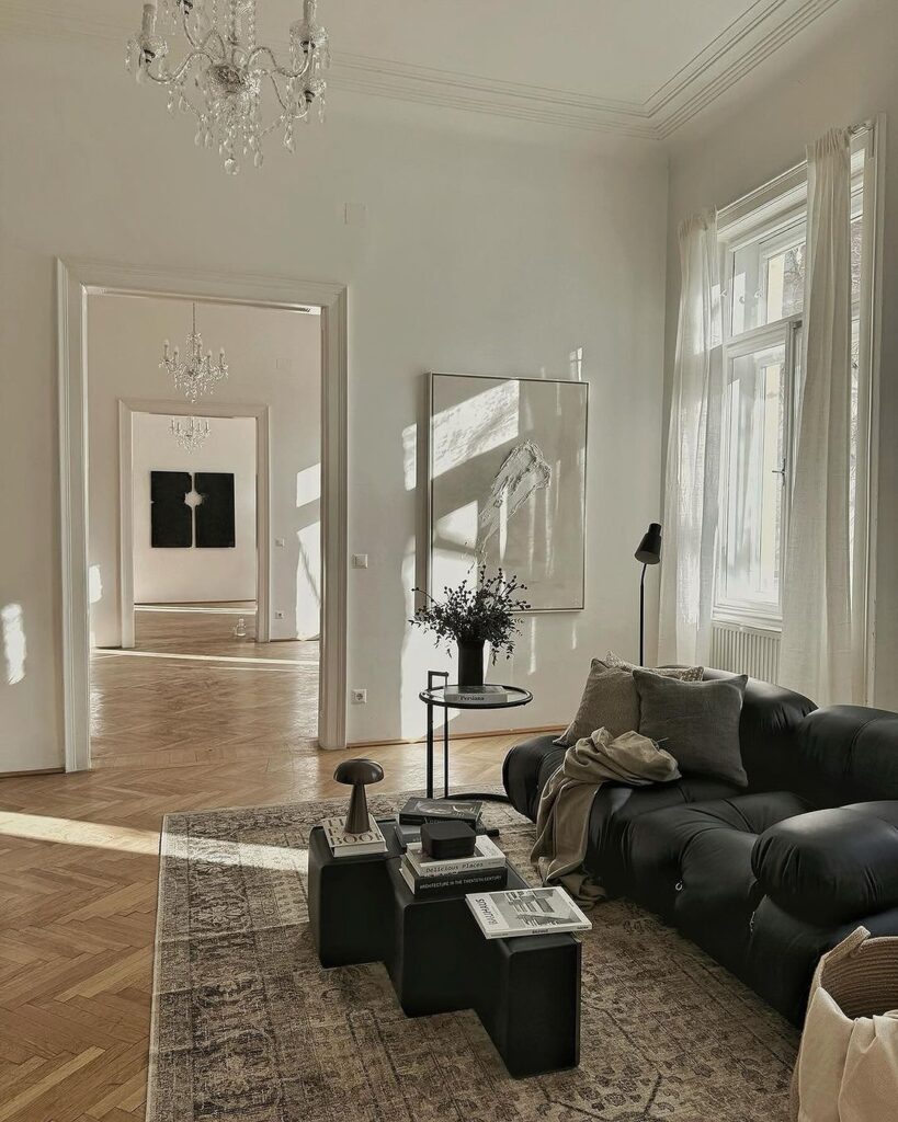 Elegant living room with black sofa, crystal chandelier, and herringbone floors.