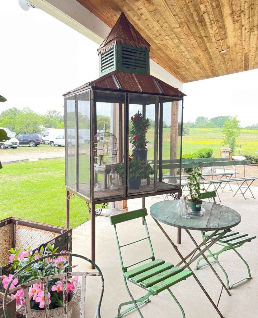 Repurposed lantern greenhouse on porch with outdoor seating and garden view.