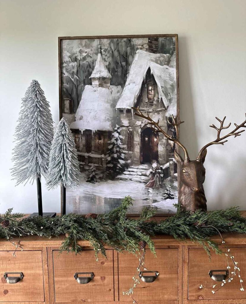 Winter cottage painting with frosted trees and reindeer on rustic cabinet