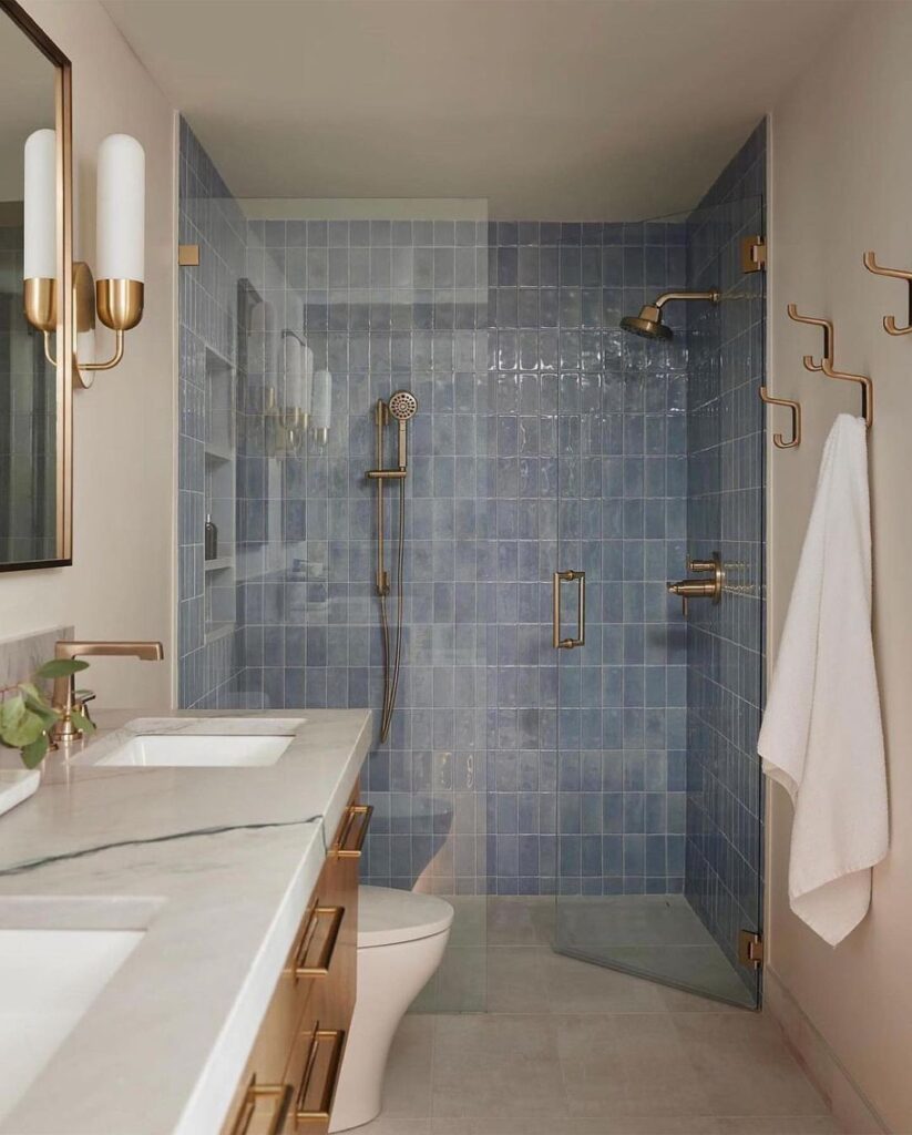 Elegant bathroom with blue-tiled shower, brass fixtures, and white vanity.