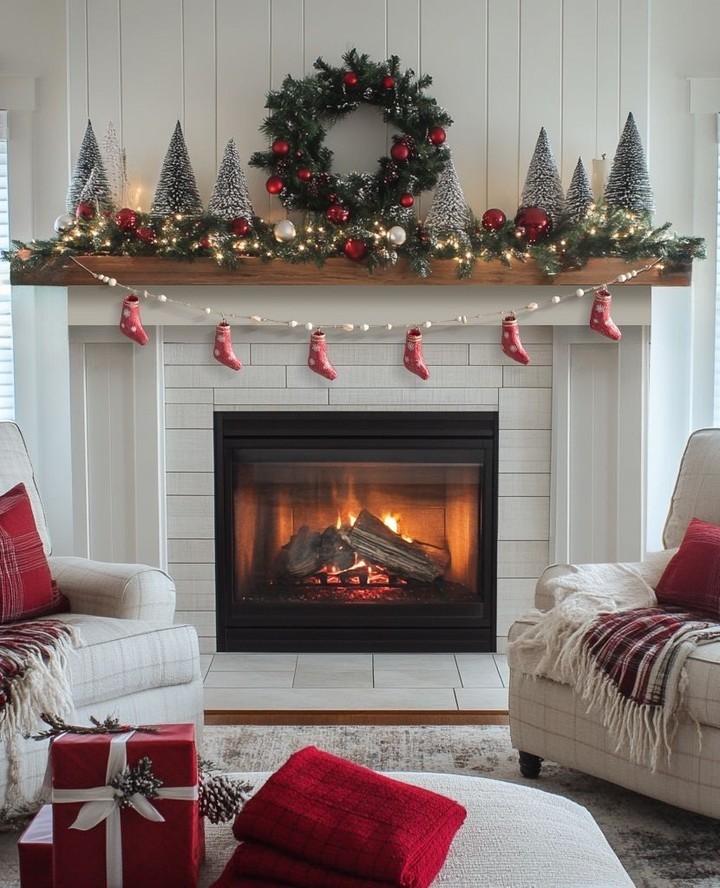 Decorated Christmas mantel with snow-covered trees and red stockings above fireplace