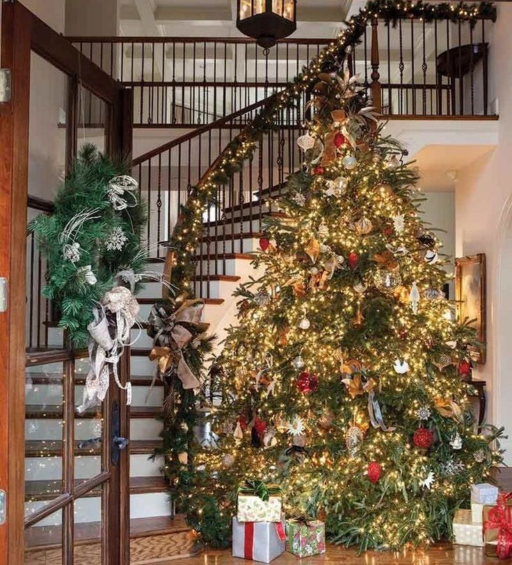 Glowing Christmas tree beside wooden staircase with iron railings and garland