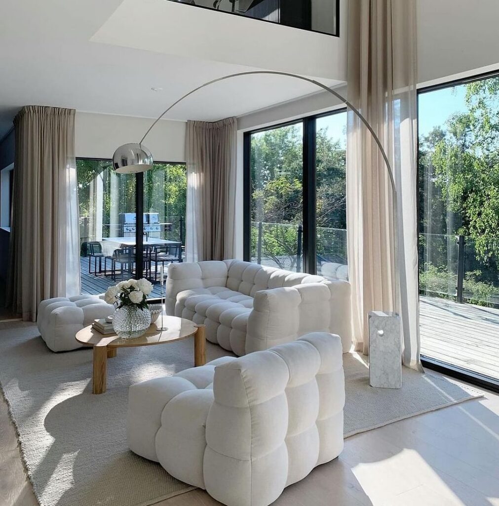 Bright living room with white sofas and large windows overlooking nature