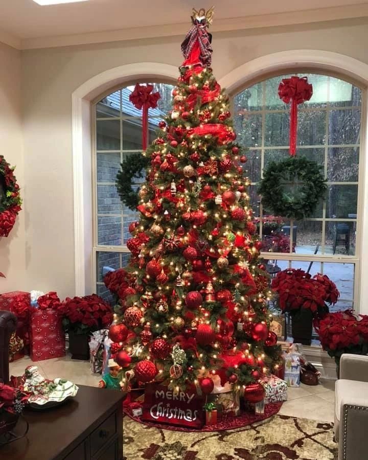 Red and gold Christmas tree with poinsettias beside arched windows