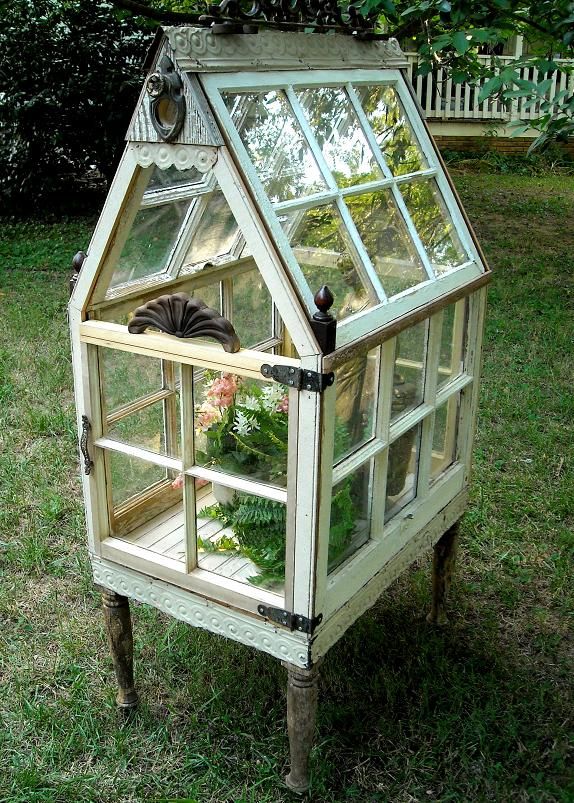 Miniature greenhouse made from old windows on wooden legs in garden