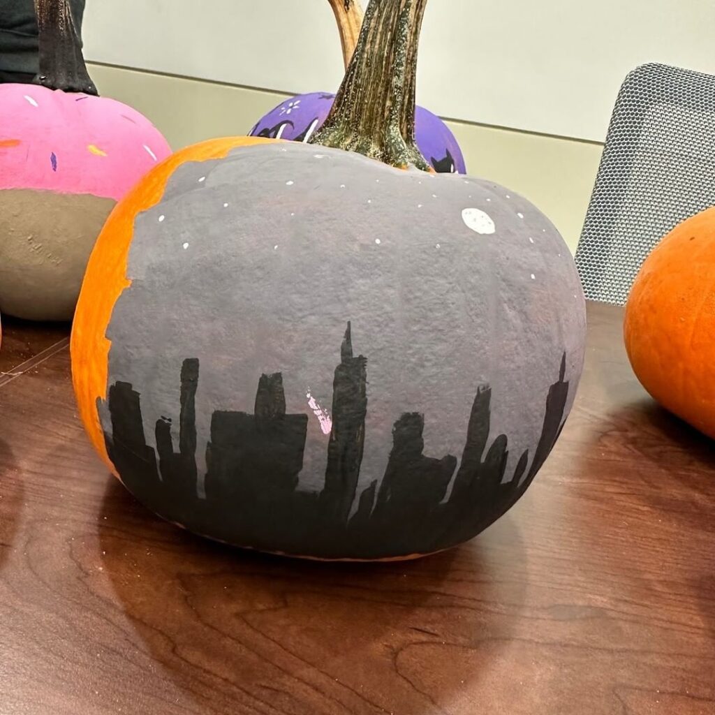 Pumpkin painted gray with black city skyline silhouette and starry sky.