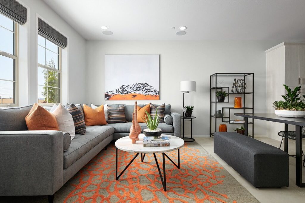 Small living room with gray sectional orange accents and mountain artwork