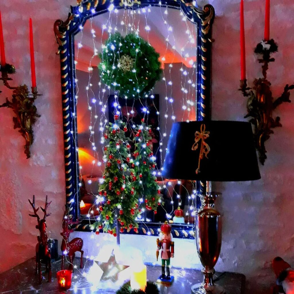 Mirror framed with fairy lights displaying Christmas tree reflection and holiday decor.