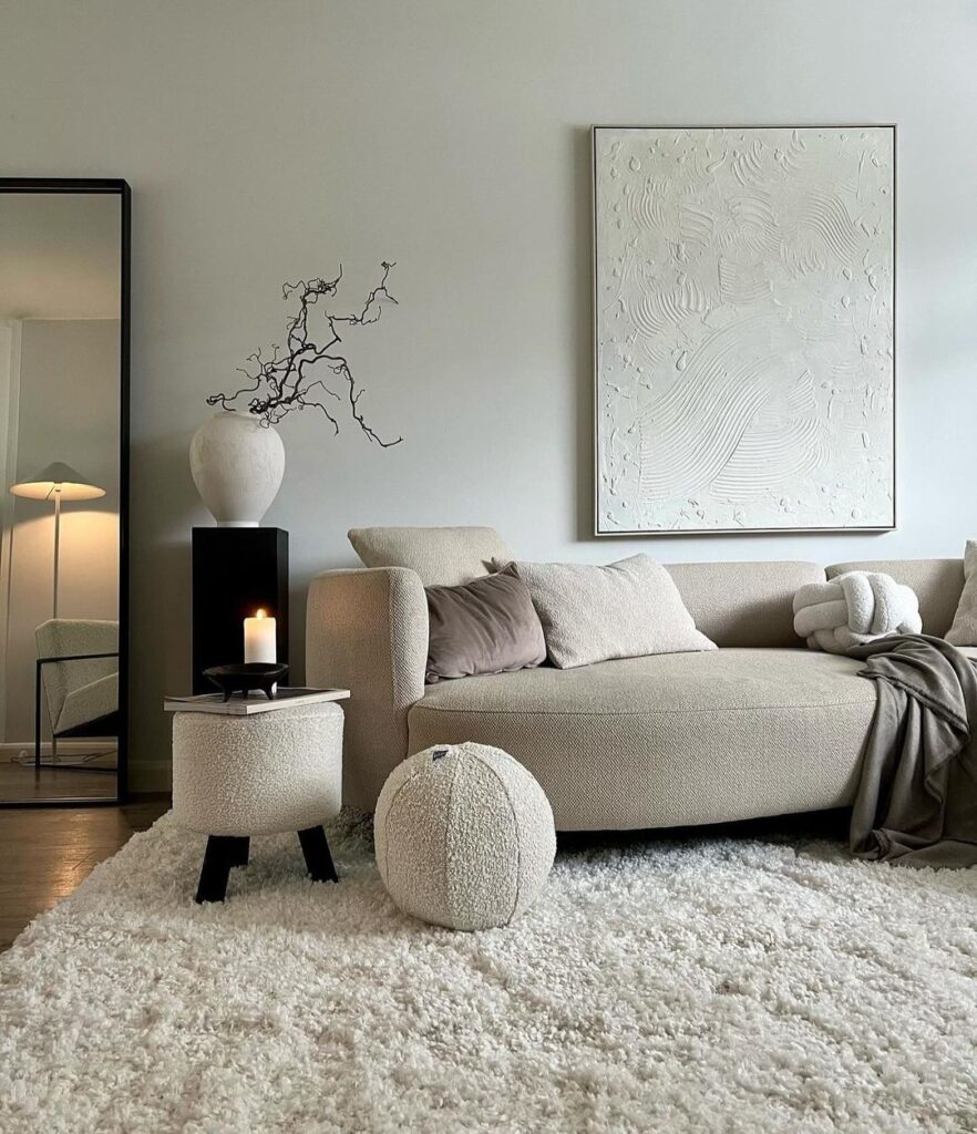 Minimalist living room with beige sofa, textured art, and cozy accessories.