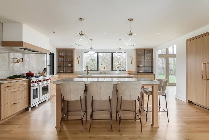 Modern kitchen with light wood cabinets globe lights and gray barstools