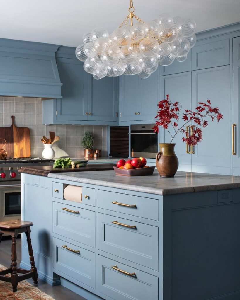 Blue kitchen island with glass chandelier marble top and brass hardware