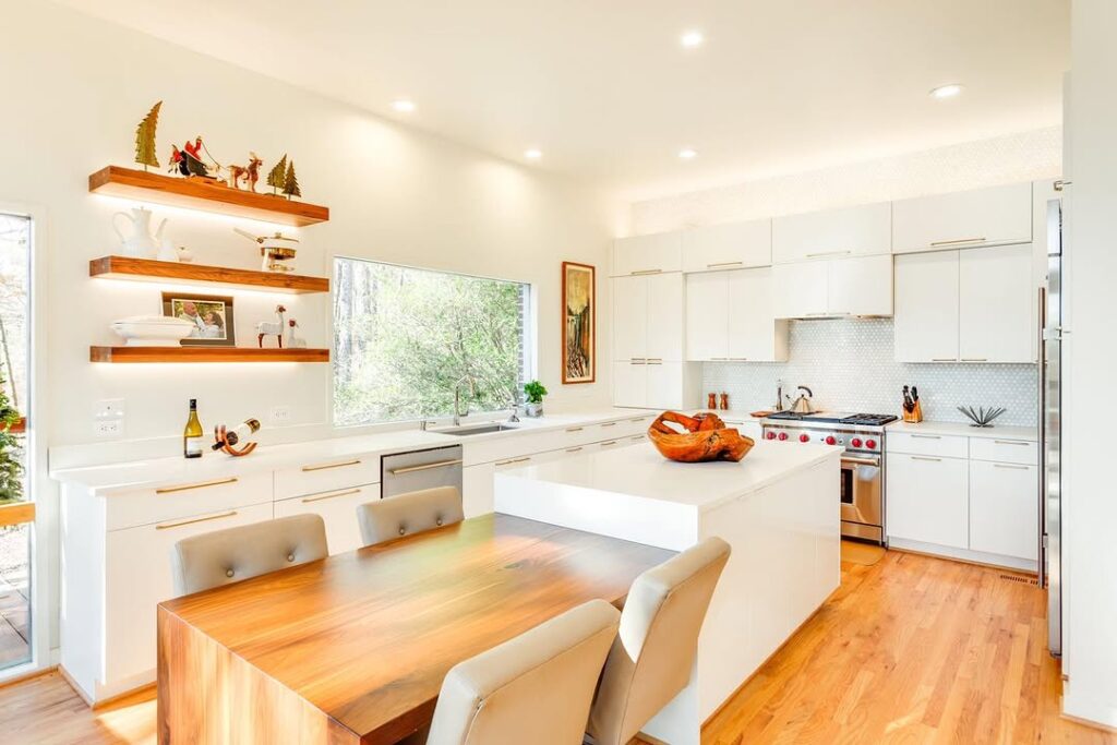 Bright white kitchen with wooden floating shelves and dining area