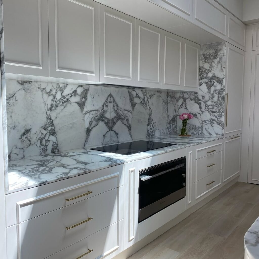 White kitchen with dramatic book matched marble backsplash and brass hardware