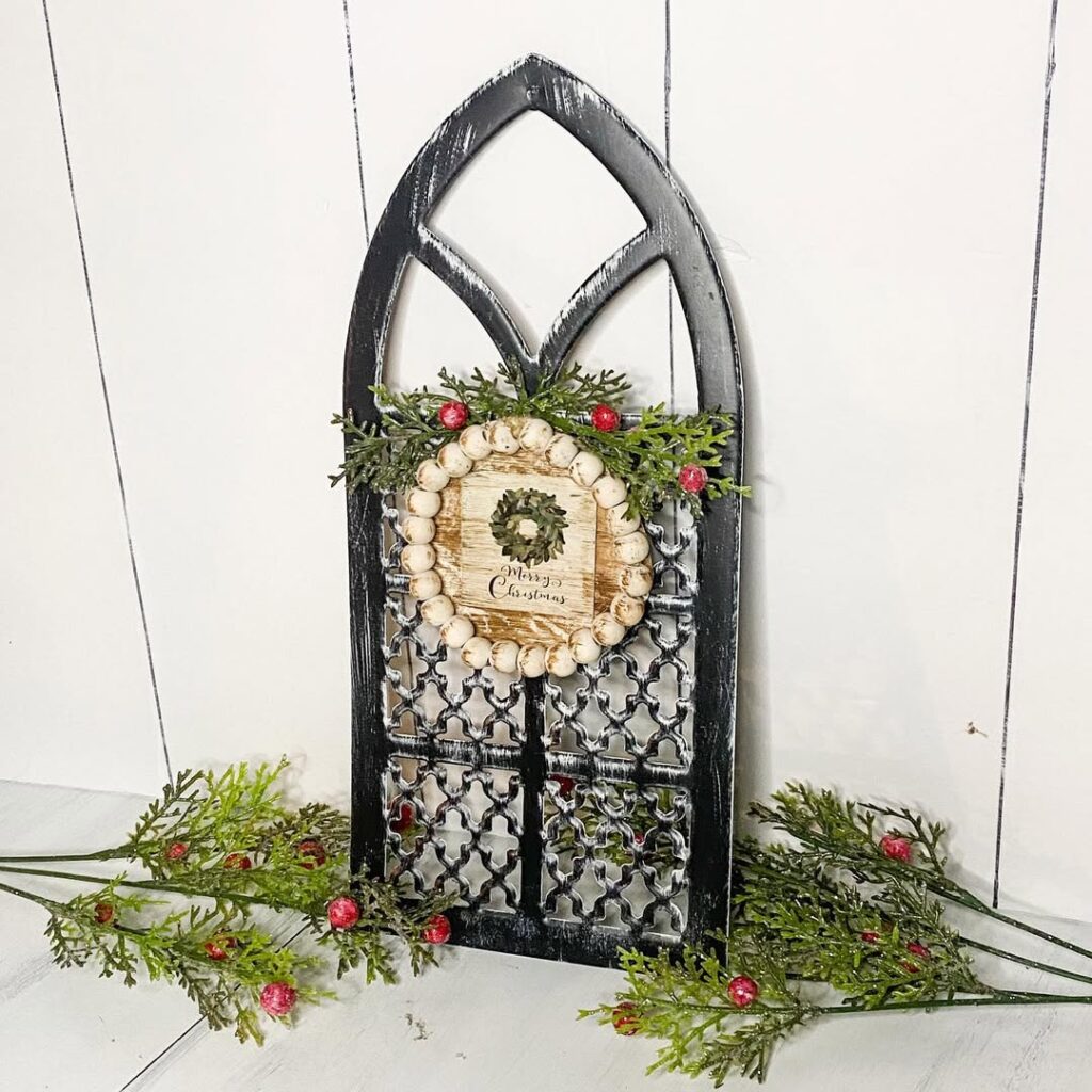 Black cathedral window frame with wooden beads and Christmas greenery