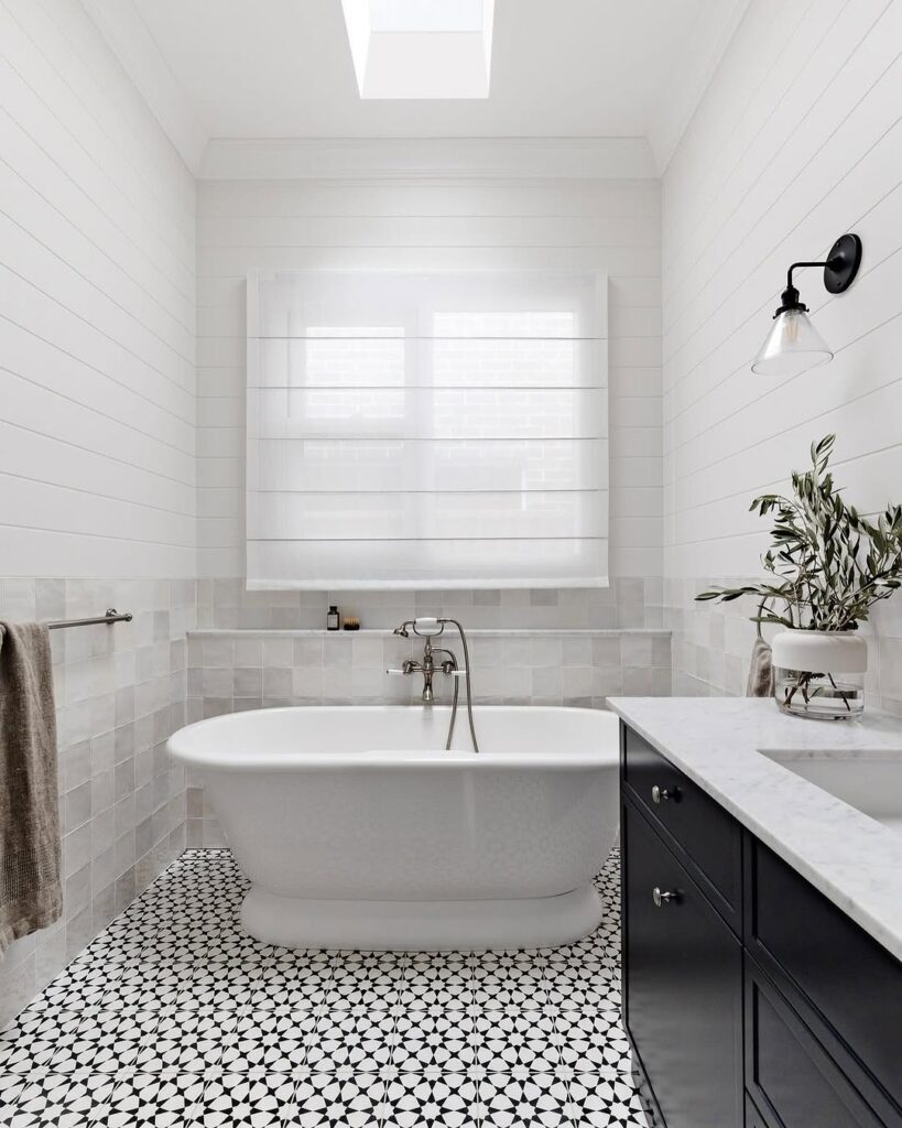 Modern bathroom with geometric tiles and freestanding tub beneath skylight