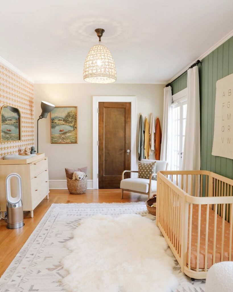 Nursery with woven pendant light natural wood crib and vintage coastal artwork on geometric wallpaper