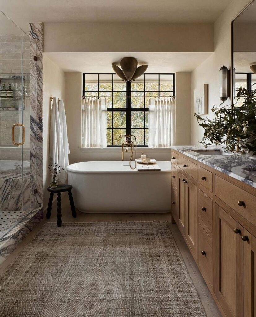  Bathroom with marble walls and oak cabinets featuring freestanding tub