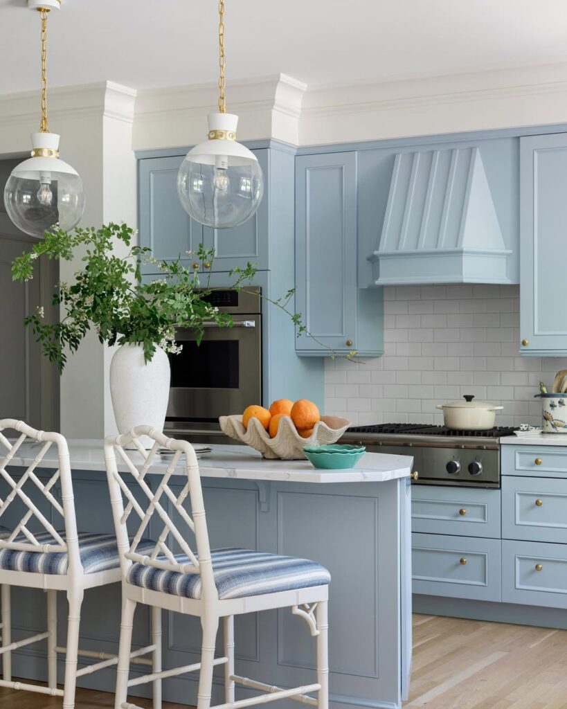 Blue kitchen with white bamboo chairs brass pendant lights and fresh greenery