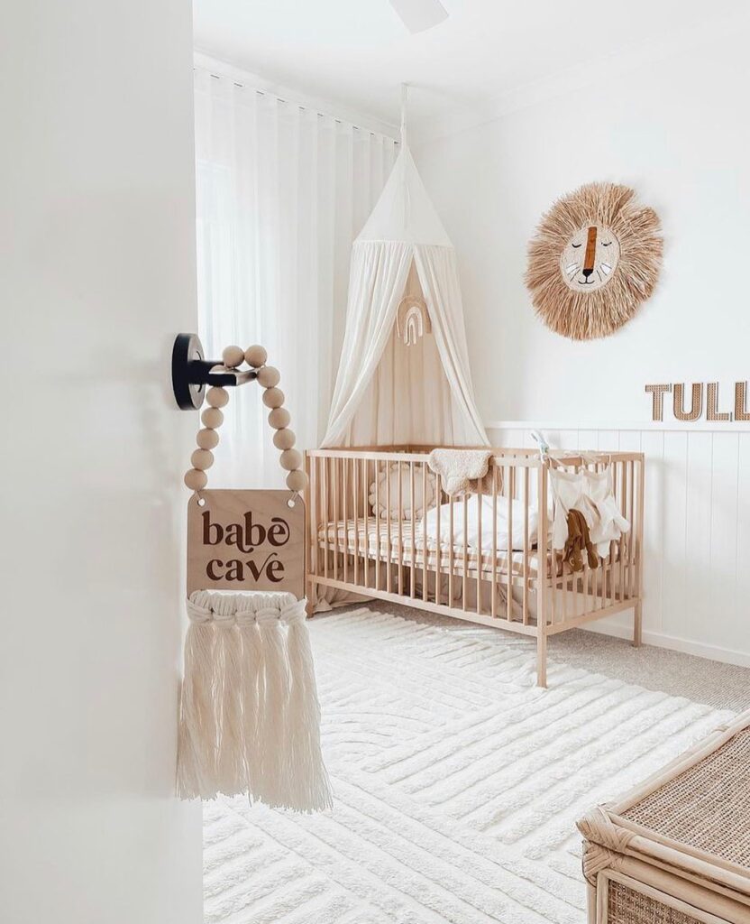 Minimalist nursery with wooden crib white canopy and macrame accents featuring babe cave sign