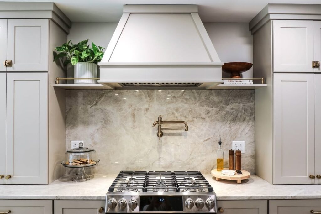 Grey kitchen with stone backsplash brass fixtures and white hood