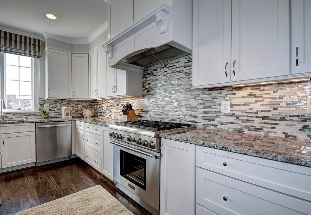 White kitchen with linear stone mosaic backsplash and granite counters