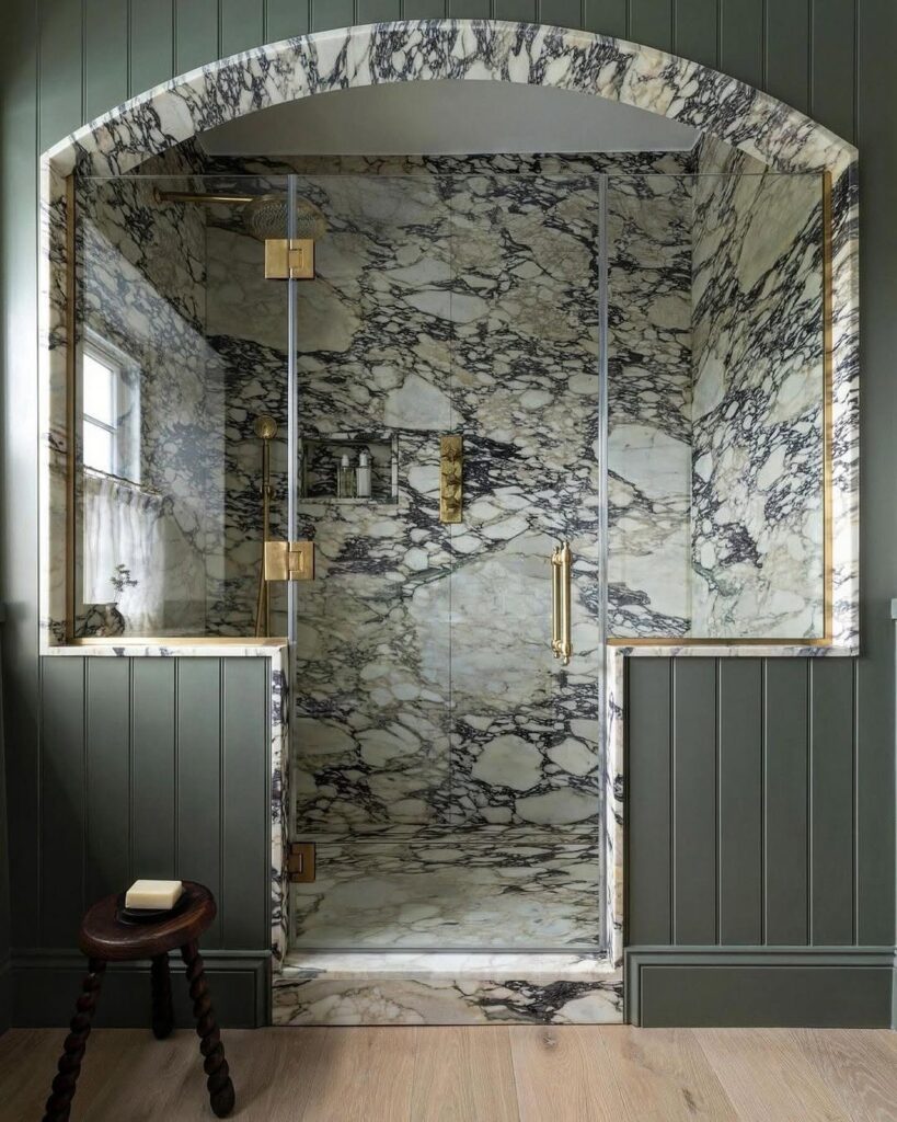 Marble shower enclosure with brass fixtures and sage green walls