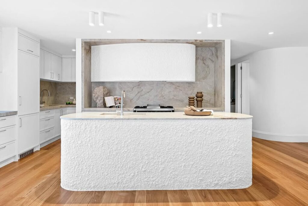 Modern white kitchen featuring curved textured island and marble backsplash