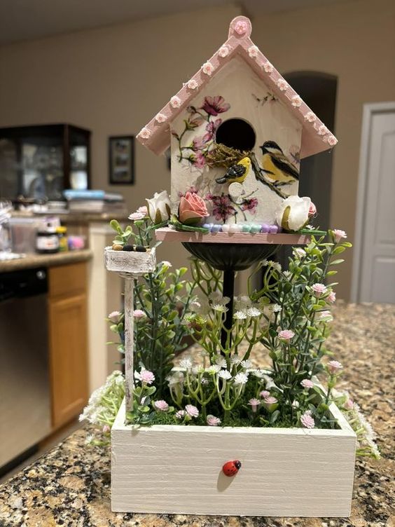 Pink birdhouse with painted birds surrounded by flowers in white box