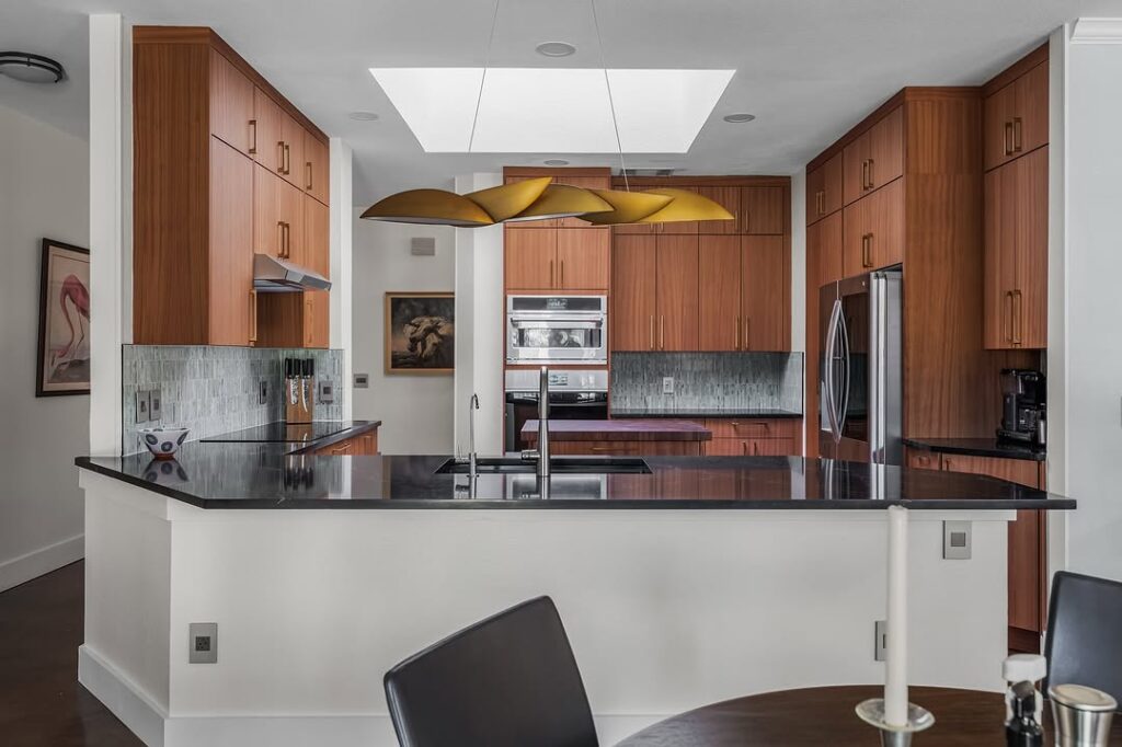 Kitchen with teak cabinets metallic pendants and black counters