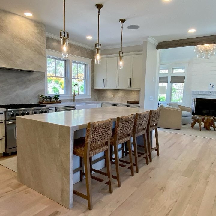 White kitchen with waterfall island woven bar stools and glass pendants