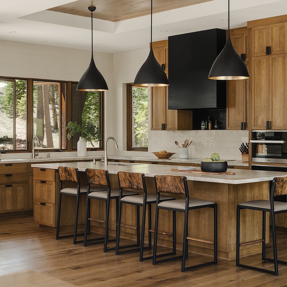 Wooden kitchen with black pendants forest views and cowhide bar stools