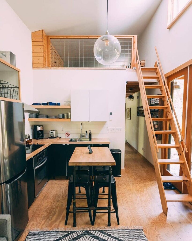 Small kitchen with black cabinets wooden countertops and loft stairs