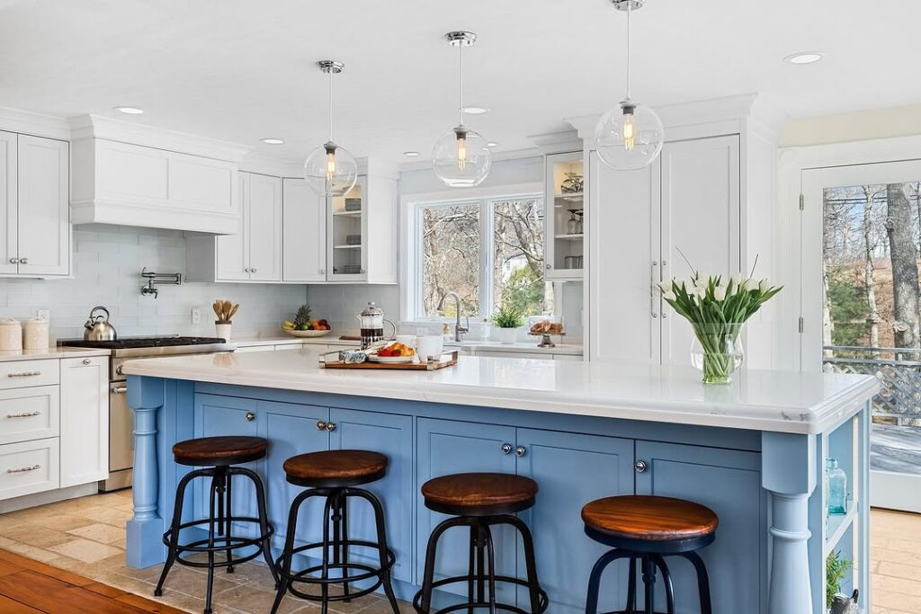  White kitchen with blue island wooden bar stools and glass pendant lights