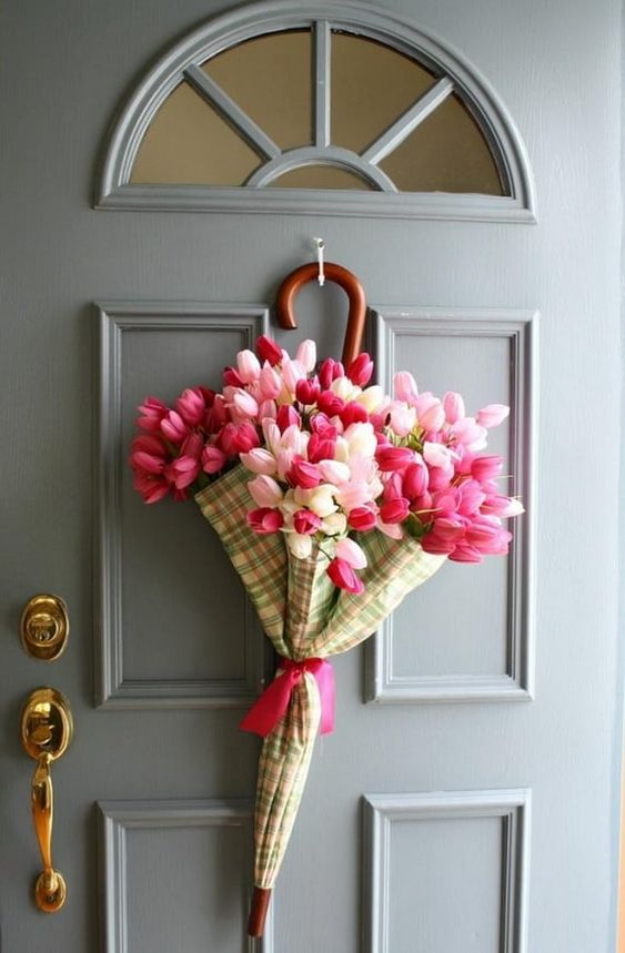 Plaid umbrella filled with pink tulips hanging on grey door