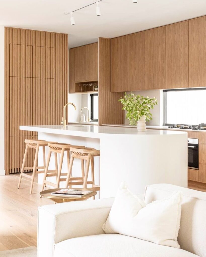 Modern kitchen featuring wooden panels and white island with natural stools