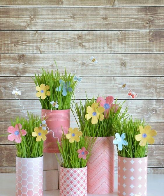 Pink paper containers with grass and paper flowers on wooden background